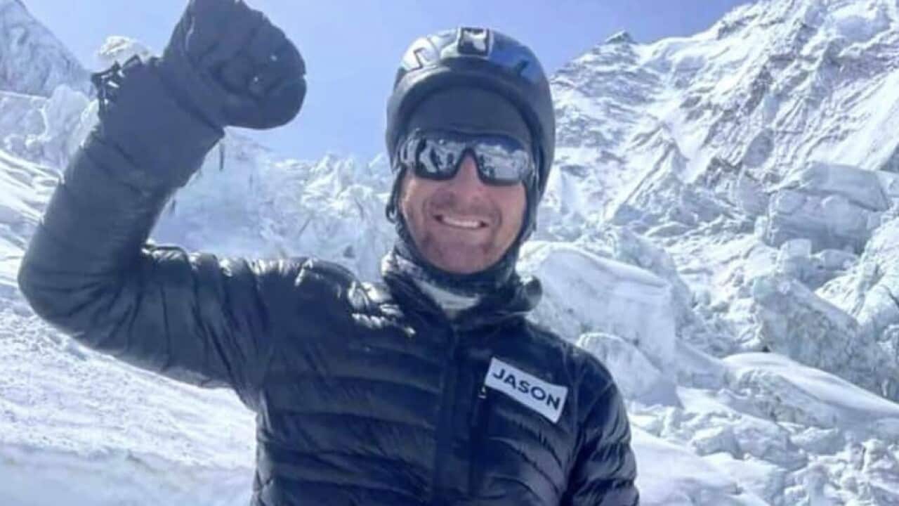 A man standing on a mountain smiling with his fist raised.