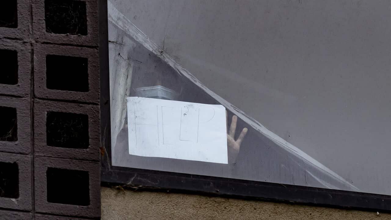 A person holds up a sign reading ‘help’ from a window of the Park Hotel in Carlton as refugee advocates rally across the road in Melbourne.