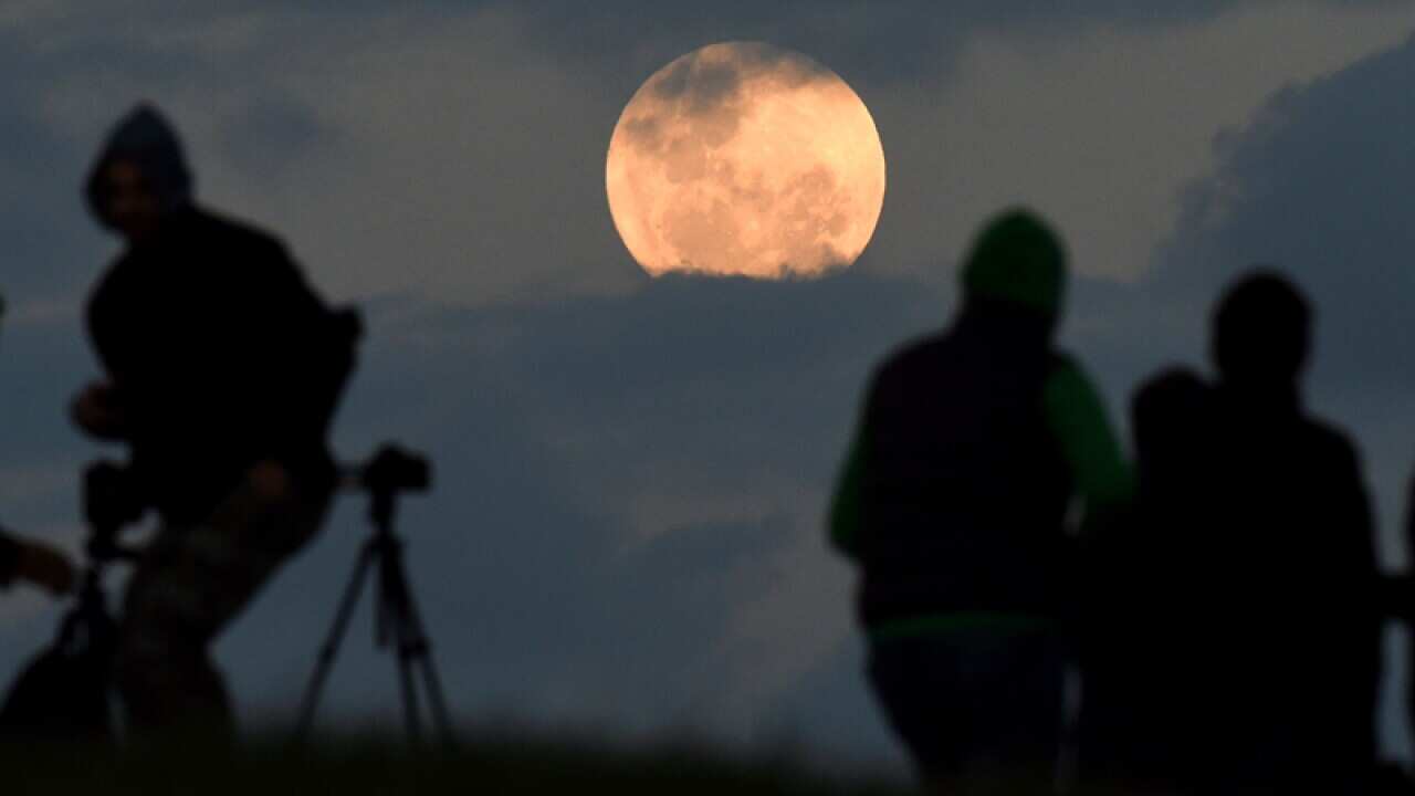 A crowd watches as the full moon is seen from Bald Hill