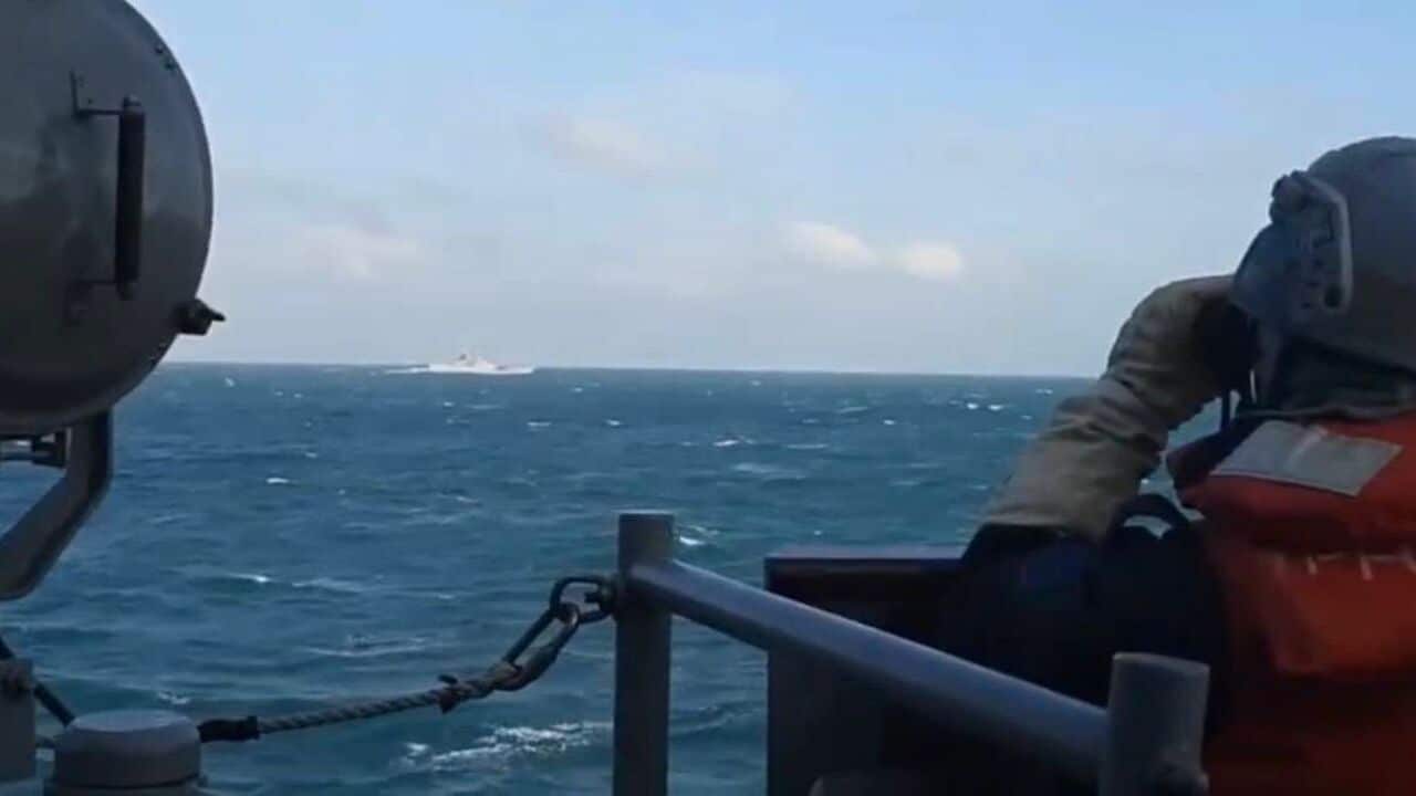 Person in a high visibility vest and helmet looking out to sea with binoculars from a boat.