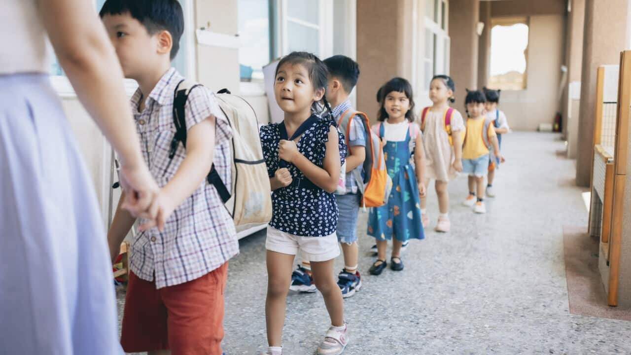 Preschool teacher guiding and arranging students waiting in line entering classroom