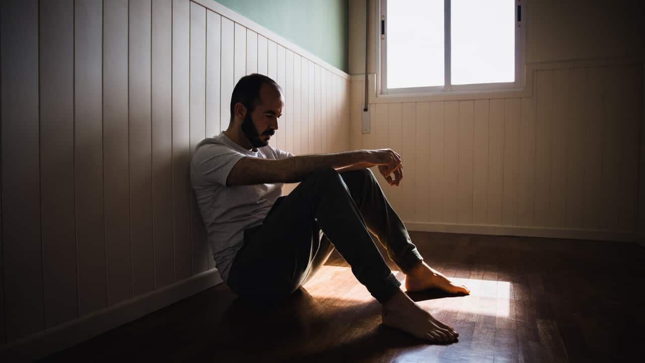 Lonely man sitting on floor by wall in dark room feeling sad