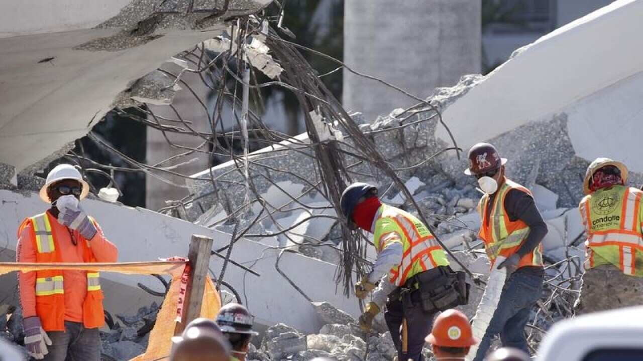 Workers remove debris from the collapsed pedestrian bridge