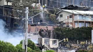 Damage from a bushfire as emergency workers can be seen hosing down buidilngs.