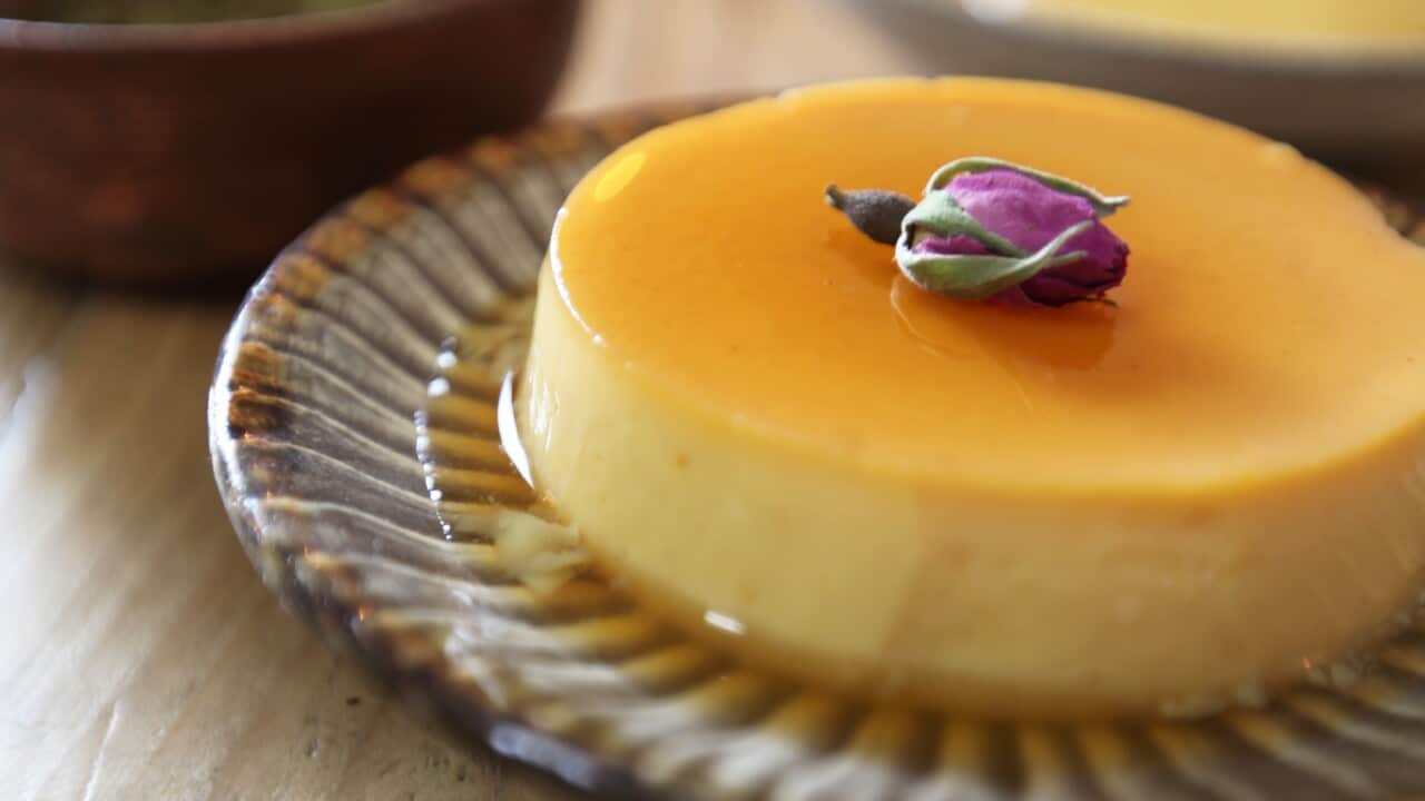 A round crème caramel, covered in a thin caramel sauce, sits on a plate with a decorative striped edge.