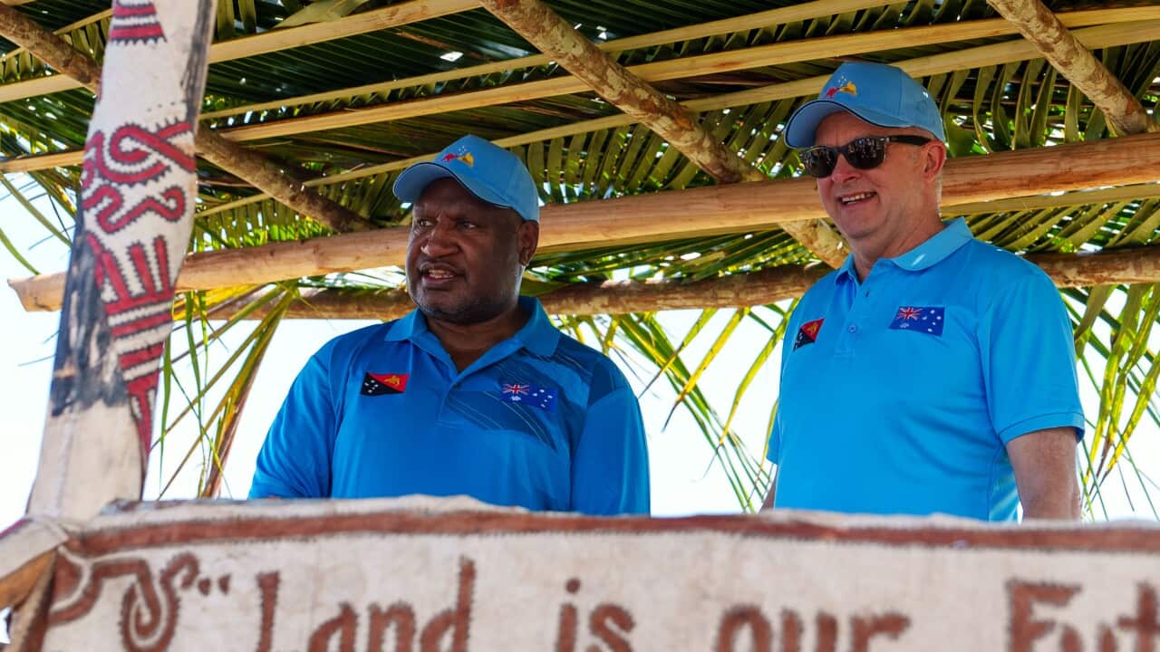 James Marape (left) and Anthony Albanese (right), both wearing blue polo shirts, pose for a photo on a raised platform.