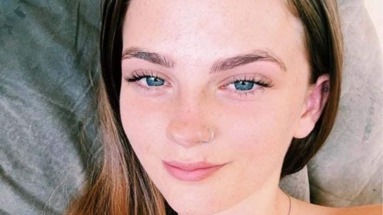 A selfie of a smiling teenage girl with long light brown hair.