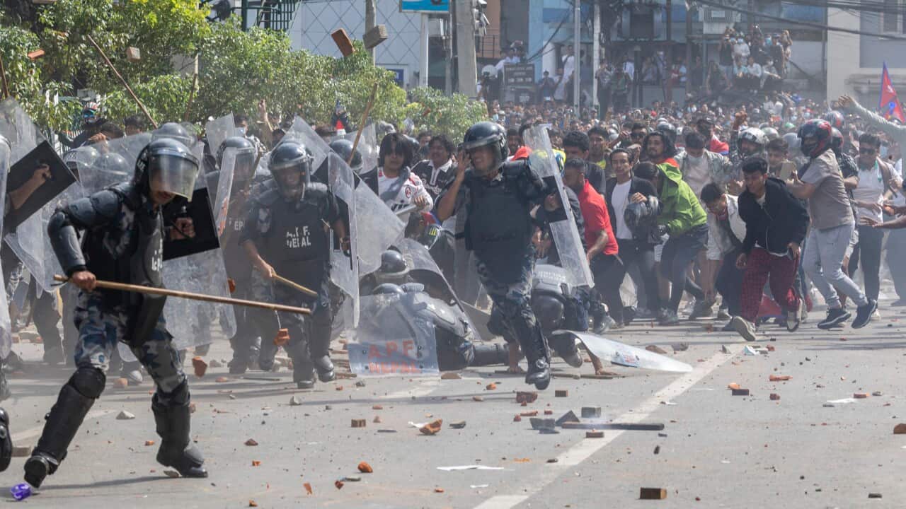 Police in riot gear clashing with protesters on a street.