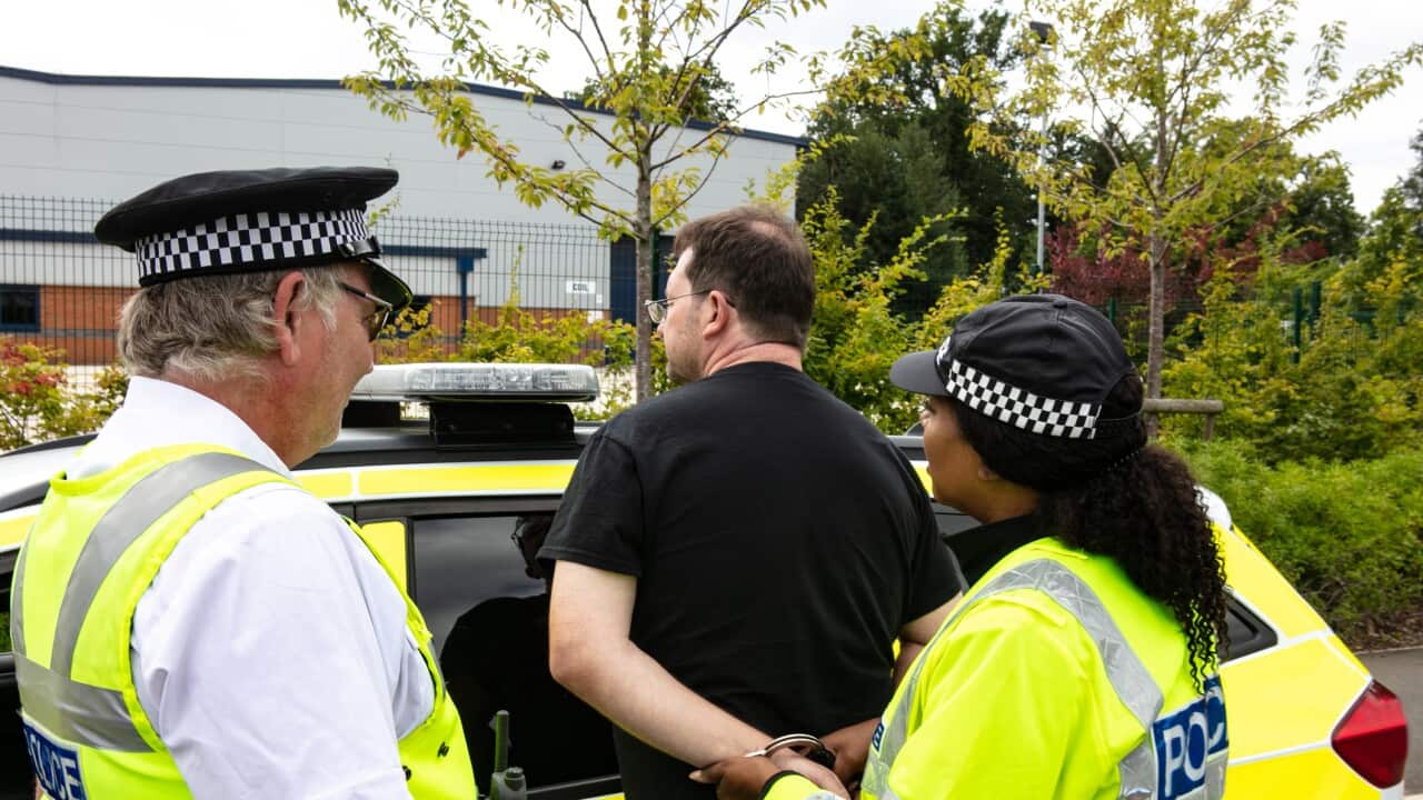Police women putting on Handcuffs on suspect by side of a Police car with another officer