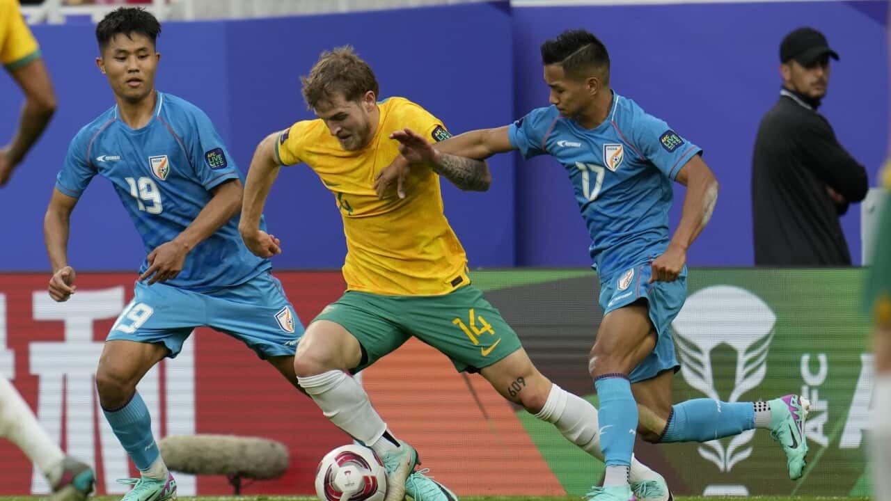 Two football players in blue jersey defend against another football player in yellow jersey with the ball.