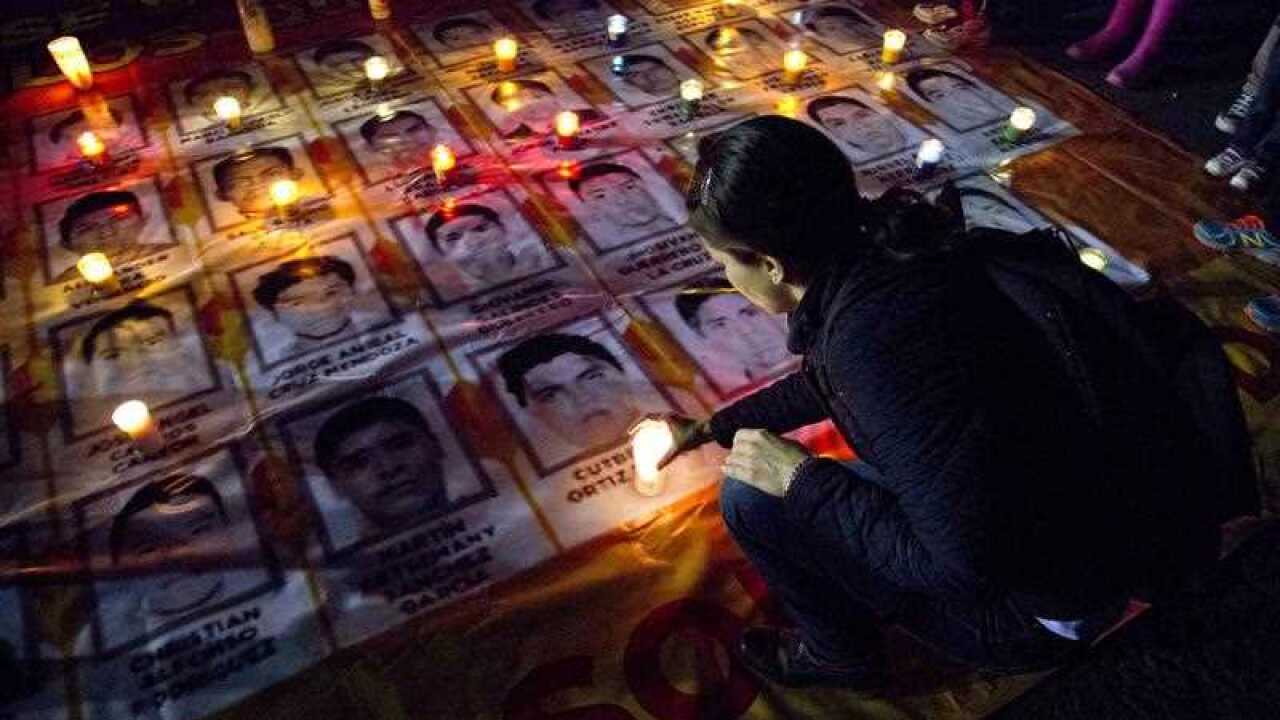 A woman places a candle among images of the missing students at a protest demanding their return. Mexico City, October 2014