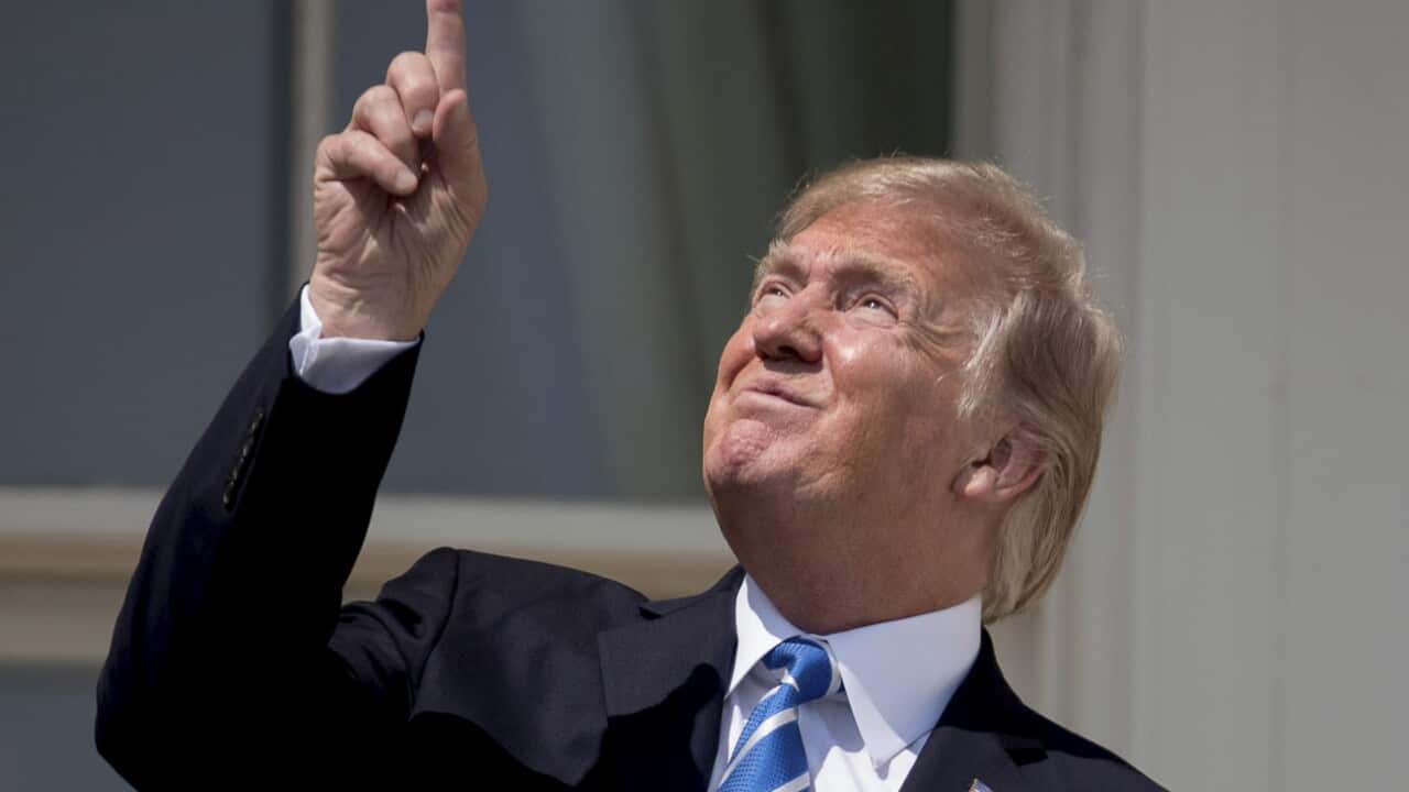 US President Donald J. Trump (R), with First Lady Melania Trump (not pictured), looks toward the sun during the solar eclipse from the balcony of the White House
