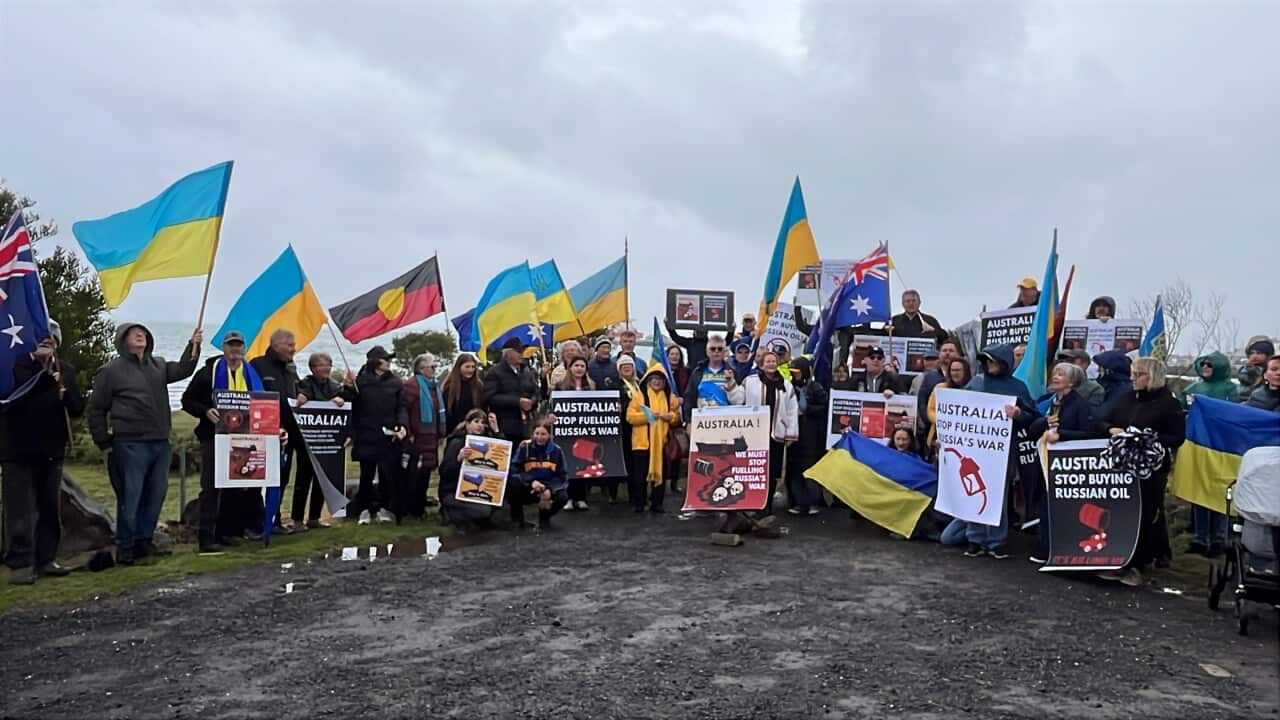 A group of people holding signs standing on concrete against a grey sky