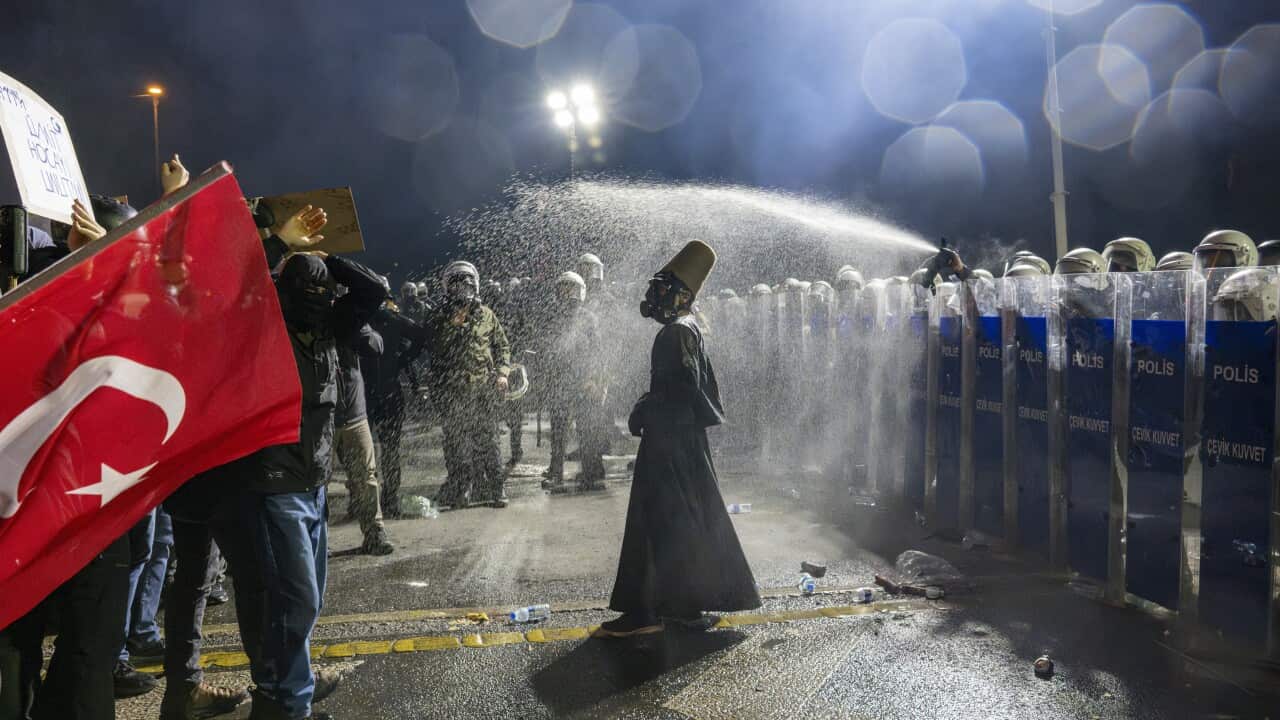 Person stands in front of police barricade in middle of road as police officers use pepper spray