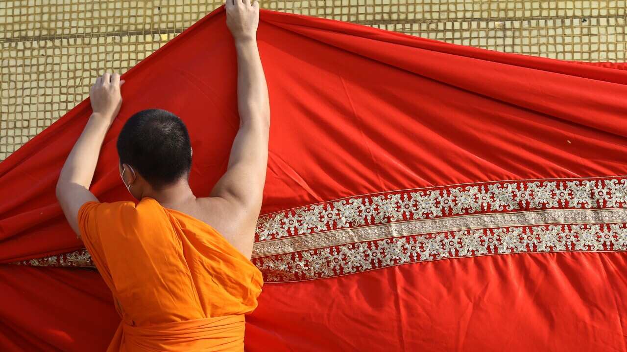A monk wrapping a structure in red cloth.