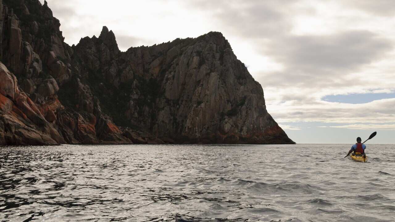 A sea kayaker paddles around sea cliffs on Schouten Island, Freycinet National Park, Tasmania, Australia.