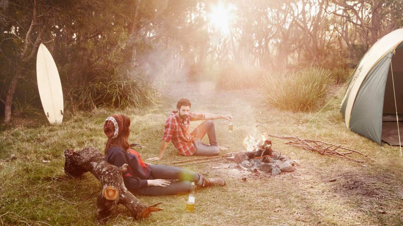 Couble camping around smokey fire on sunset