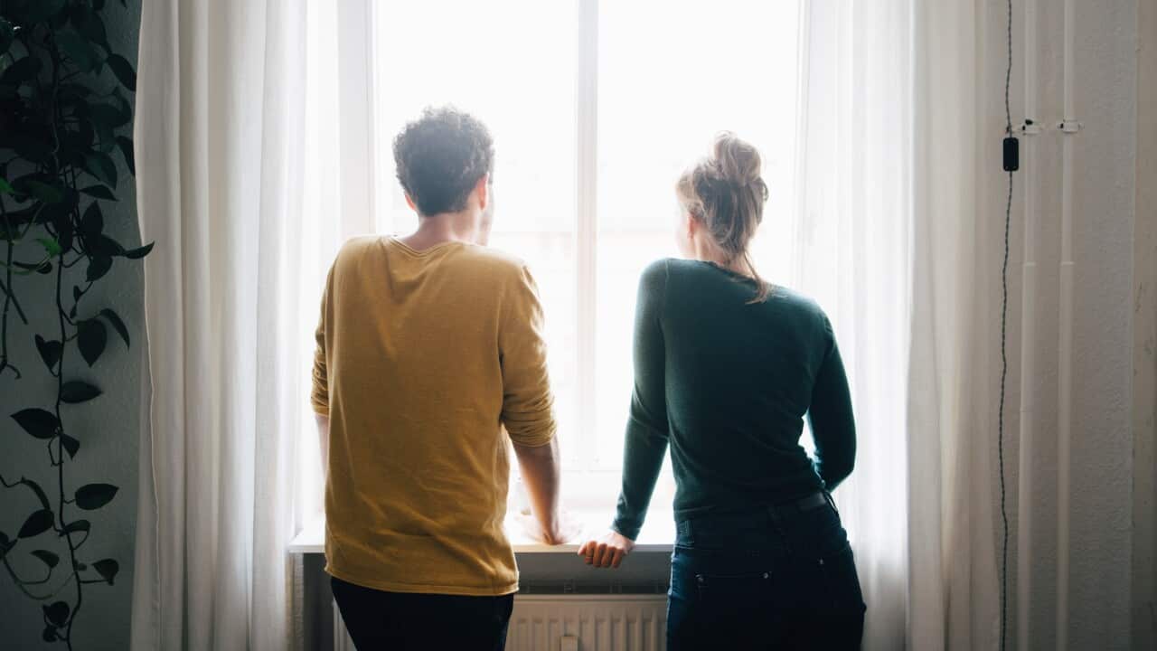 Rear view of couple looking through window while standing at home