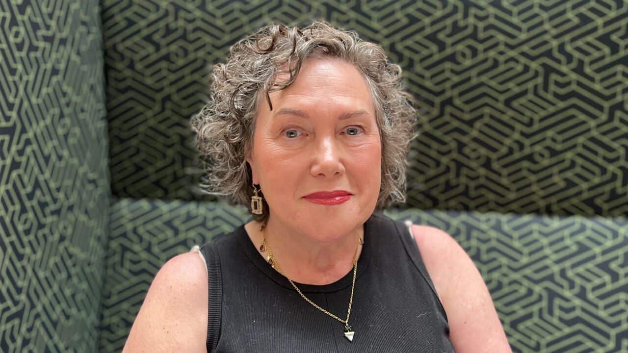 A close-up shot of a middle-aged woman with grey hair sitting on a green and black geometrically patterned couch