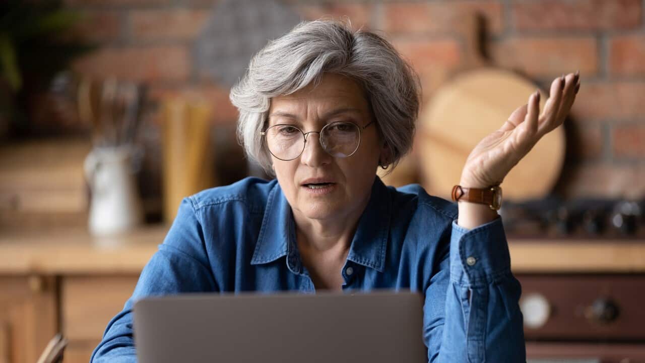 Confused middle aged woman in glasses looking at computer screen.