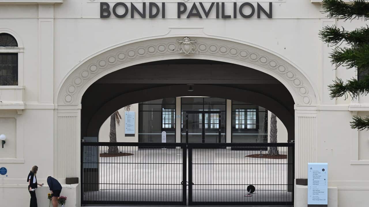 Two pepole lay flowers outside a building marked “Bondi Pavilion“.