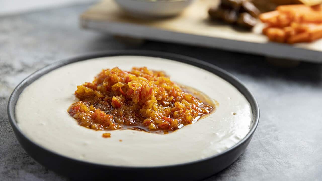 A shallow round serving dish holds a creamy white bean dip topped with a chunky reddish chilli jam.