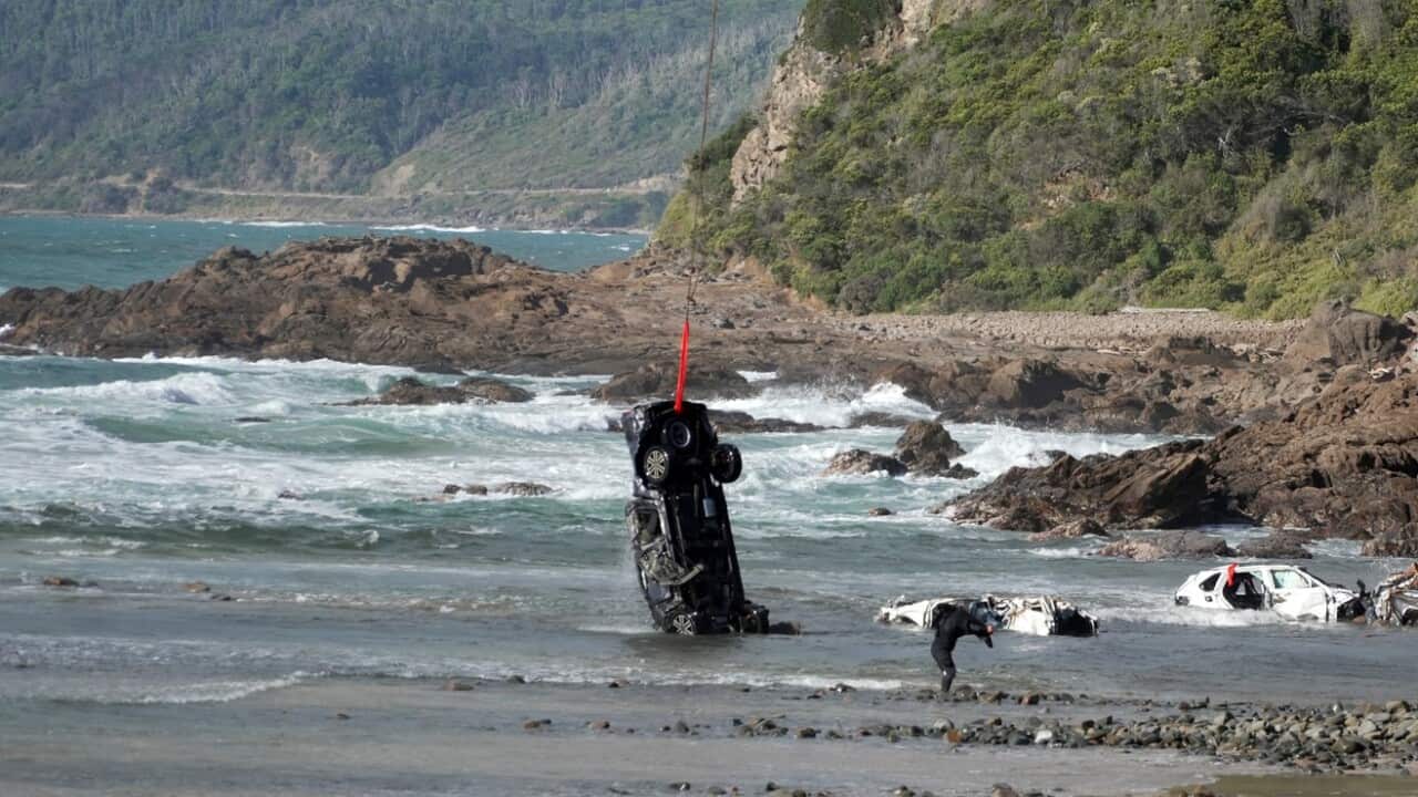 A car being winched from the ocean. The wreckage of several other cars can be seen in the water.