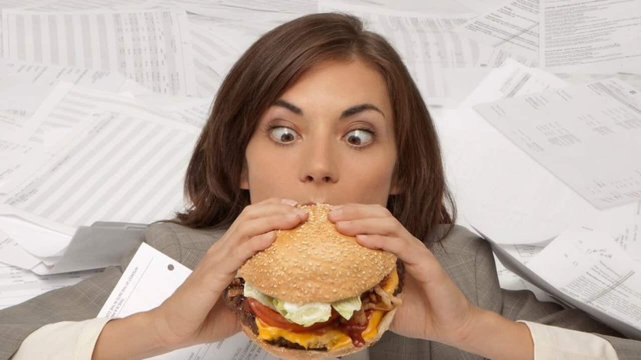 Mixed race businesswoman drowning in paperwork eating hamburger