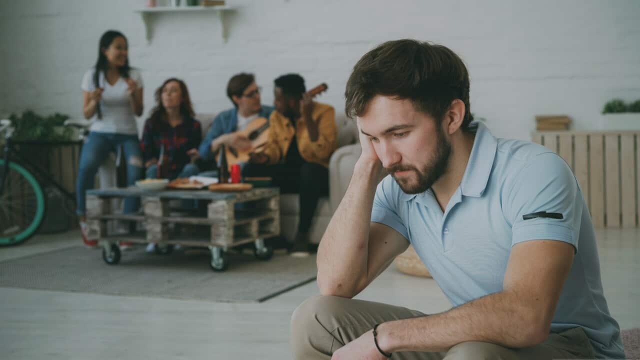 Young student guy feels upset and isolated while his friends celebrating party at home indoors