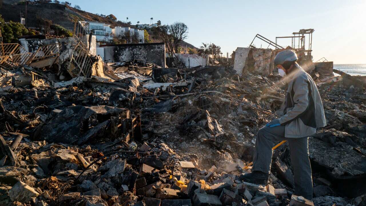A man sifting through rubble of a burnt property