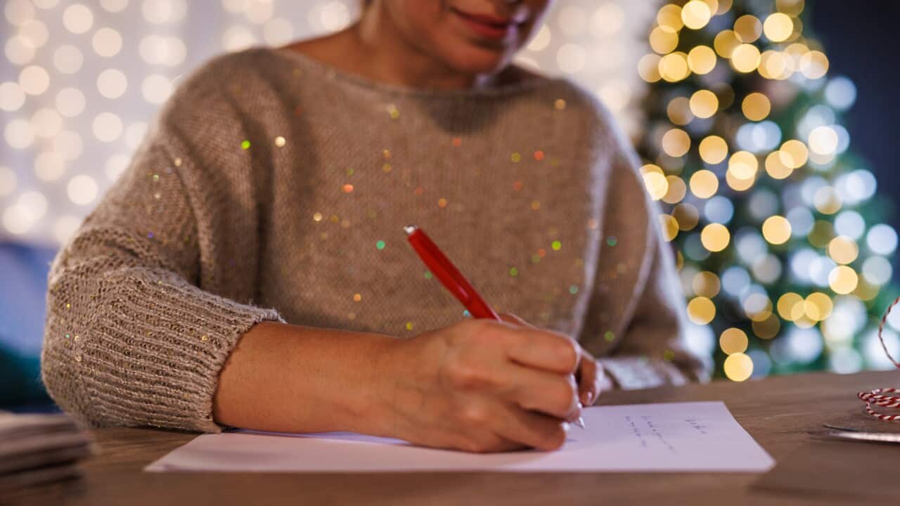 Woman sitting at the table and writing a letter for Santa for Christmas