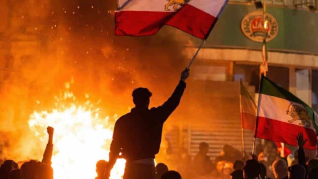 Protesters wave Iranian flags as flames light up a nighttime street during unrest.