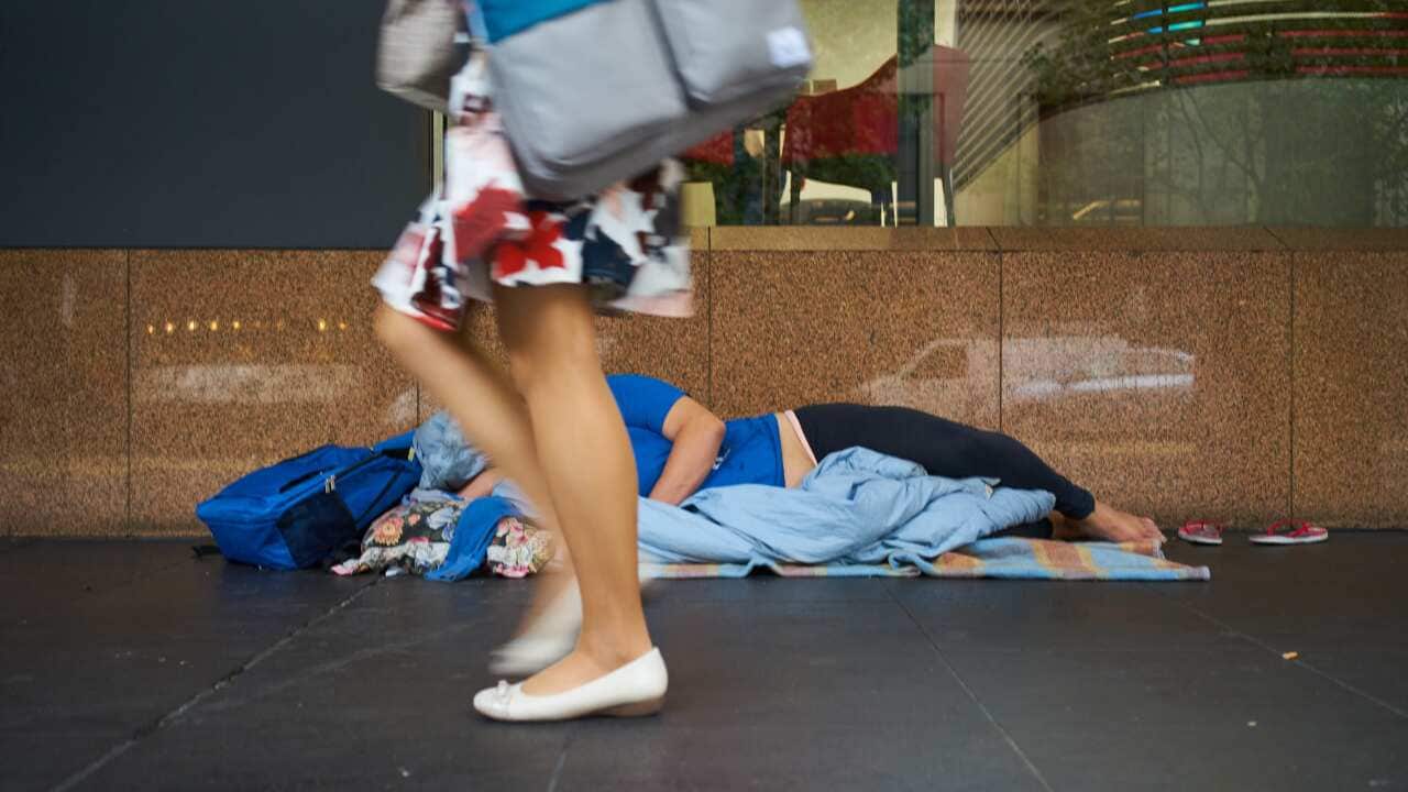 A woman walking past a homeless person sleeping on the street.