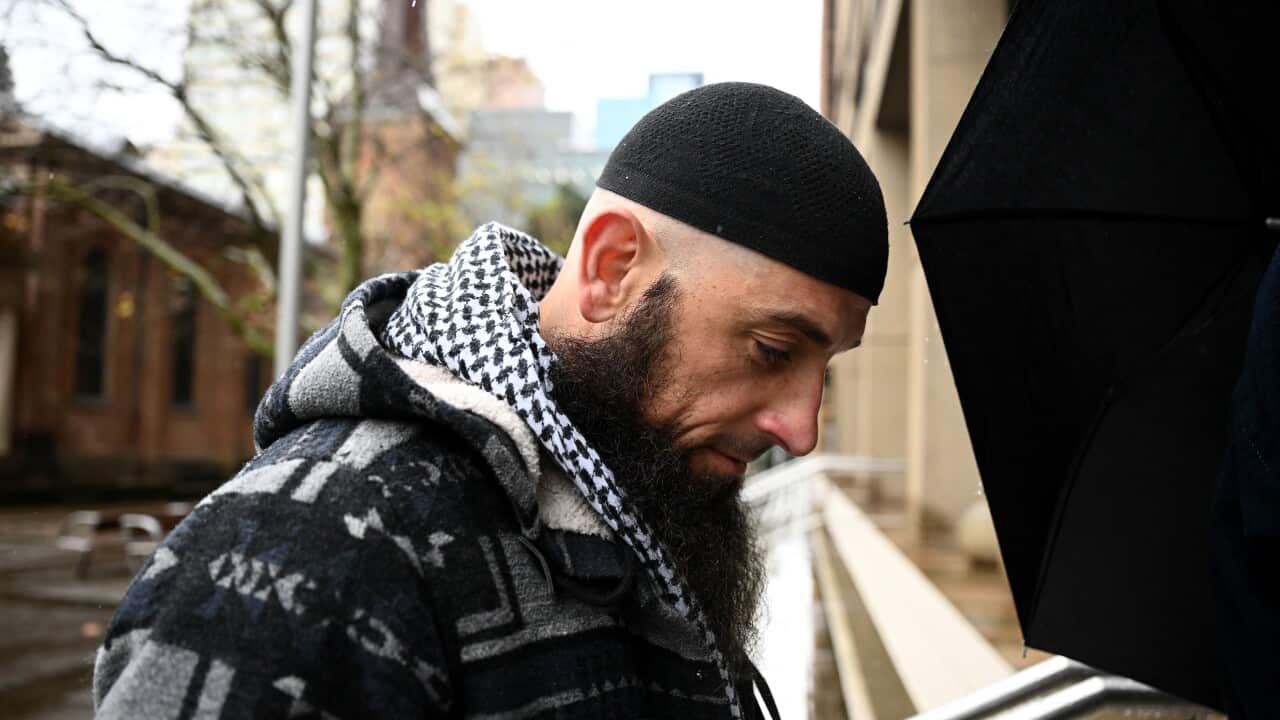 A side profile of a man with a long beard, wearing a black skull cap and a keffiyeh around his neck.