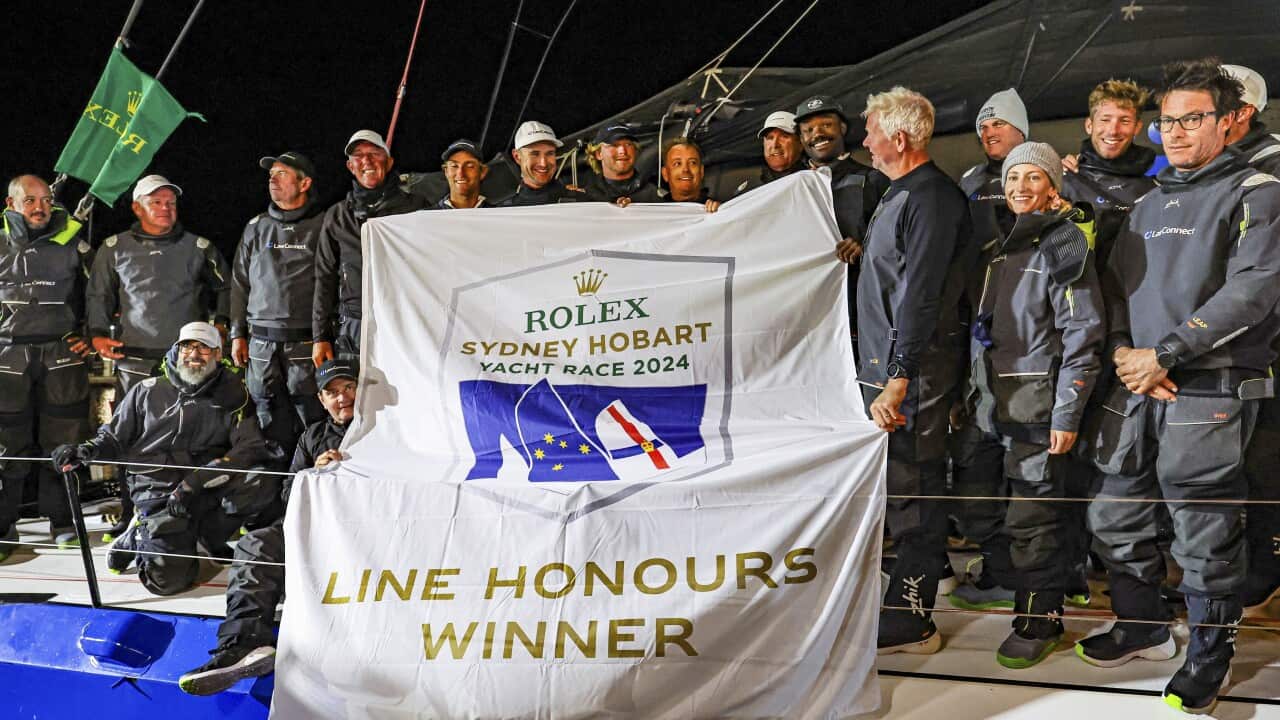 A large group of men hold up a flag on a boat that reads 'Line Honours Winner'