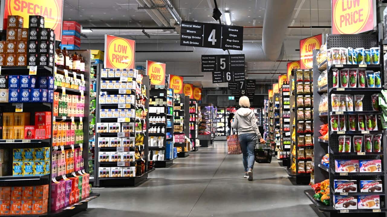 A single shopper is seen walking through a grocery store with a basket in hand.