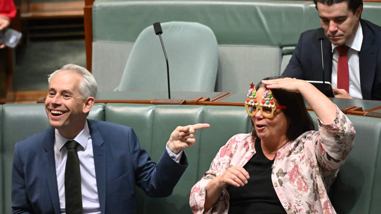 A man in a suit is laughing while pointing his finger at a woman sitting next to him, who is wearing a funny pair of glasses.