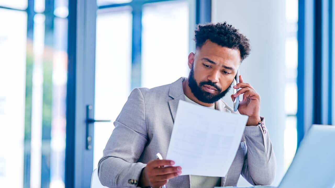 Shot of a young businessman going through paperwork while on a call at work