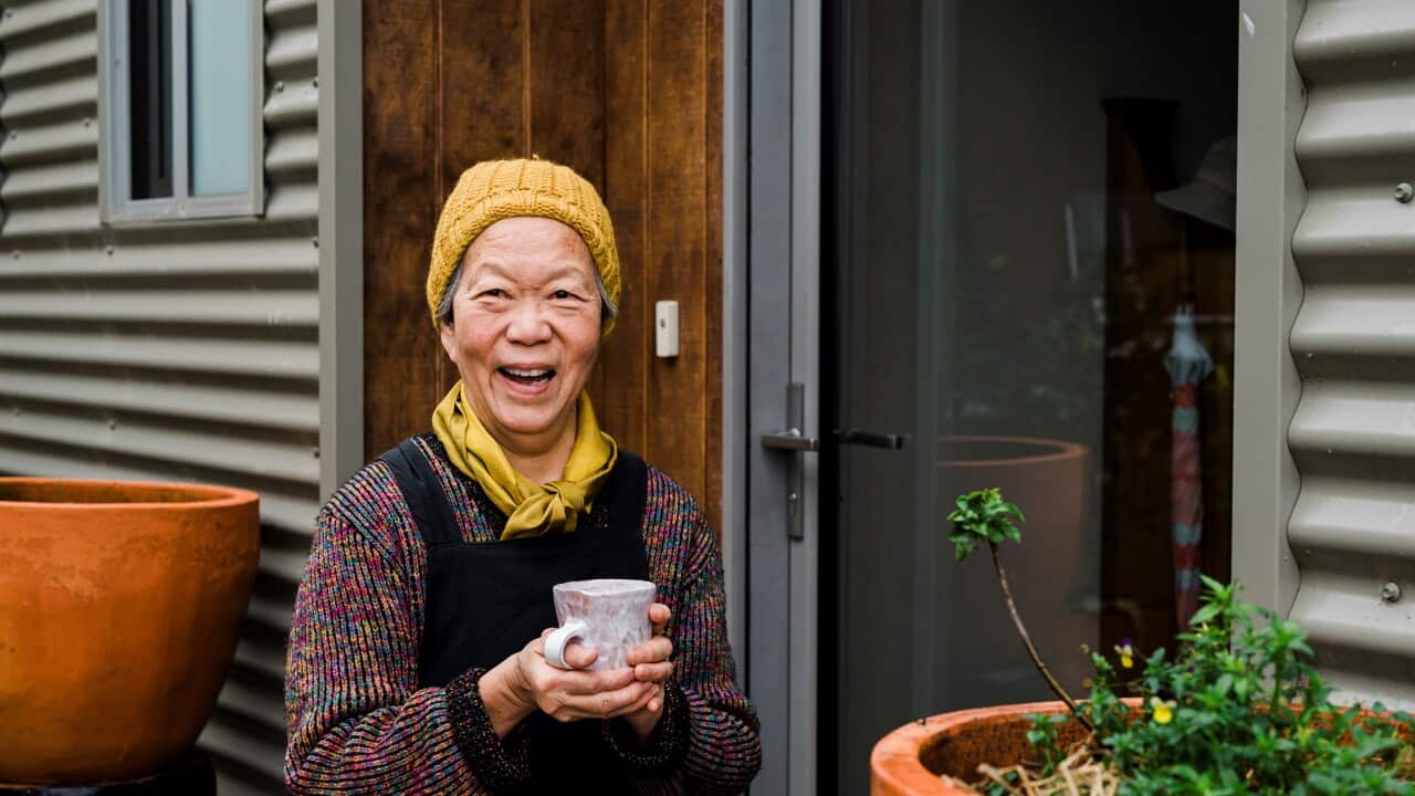 Duang holding a mug smiling at camera next to plant
