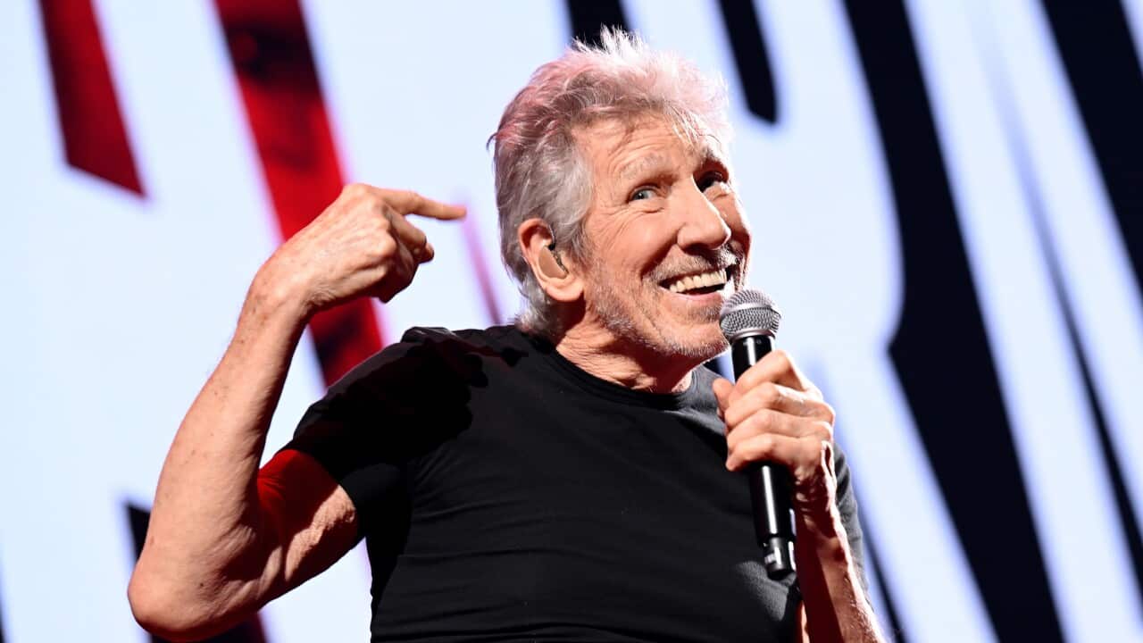 An old white man wearign a black t-shirt and holding a microphone