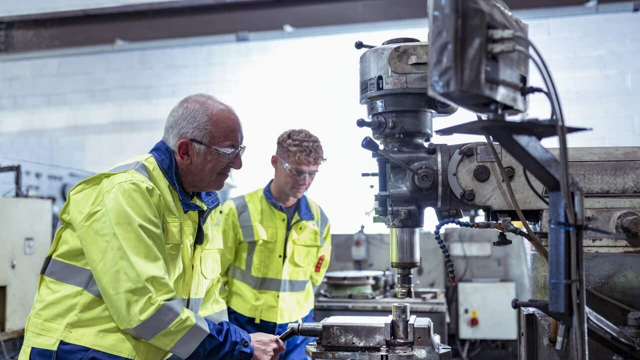 Engineer mentoring apprentice on traditional lathe in engineering factory