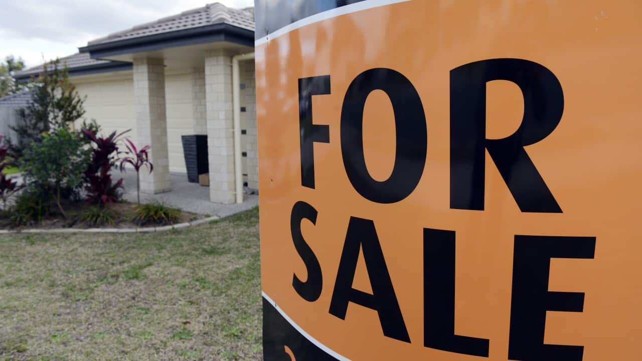 Se ve un letrero naranja que dice «Se vende» frente a una casa suburbana estereotipada. 