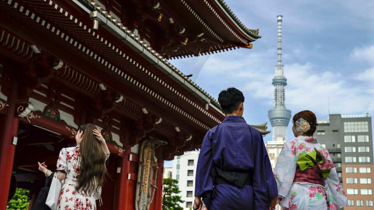 A couple wearing kimono's holds hands as they walk into a temple.