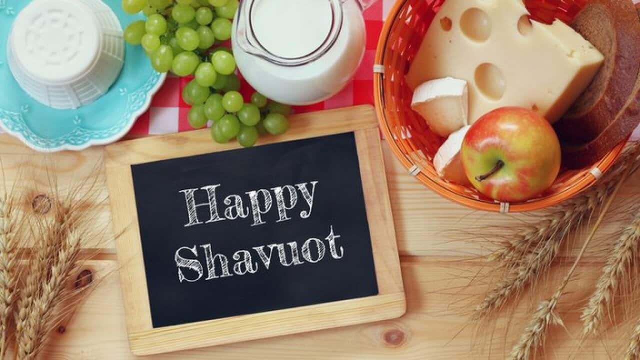 image of dairy products and fruits next to blackboard with the phrase: HAPPY SHAVUOT, on wooden background. Symbols of jewish holiday - Shavuot
