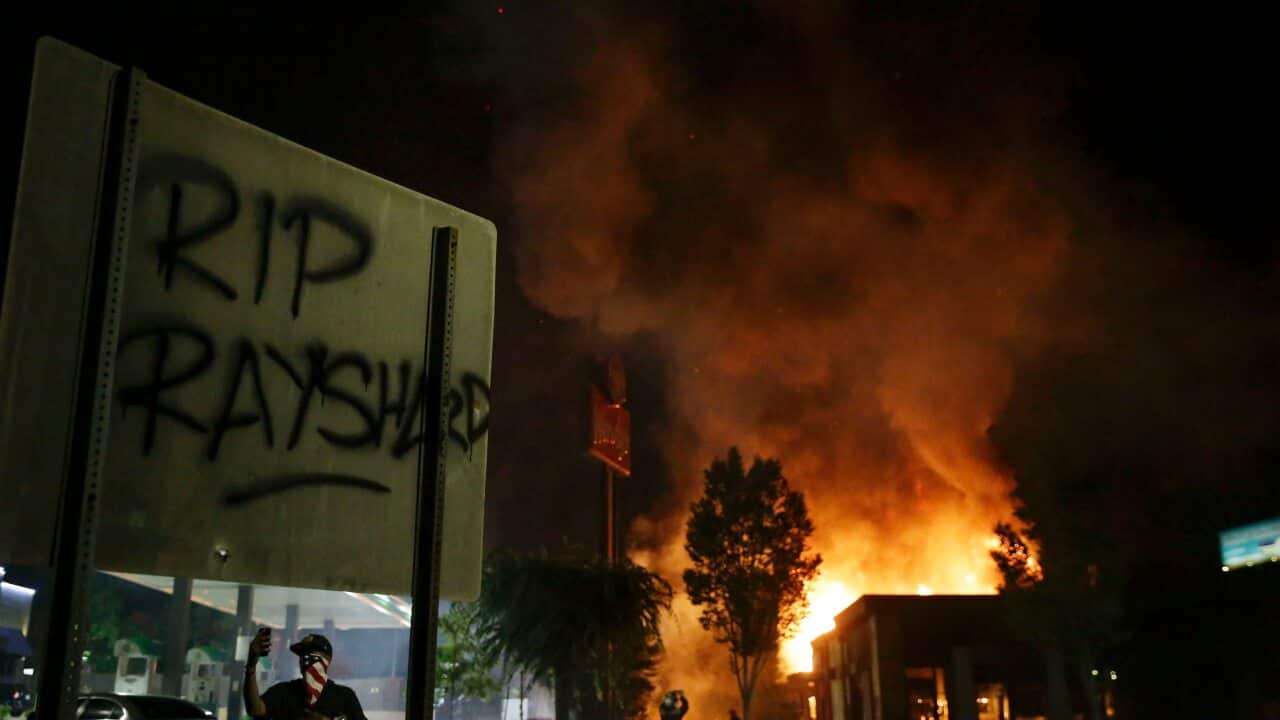 "RIP Rayshard" is spray painted on a sign as as flames engulf a Wendy's restaurant during protests.