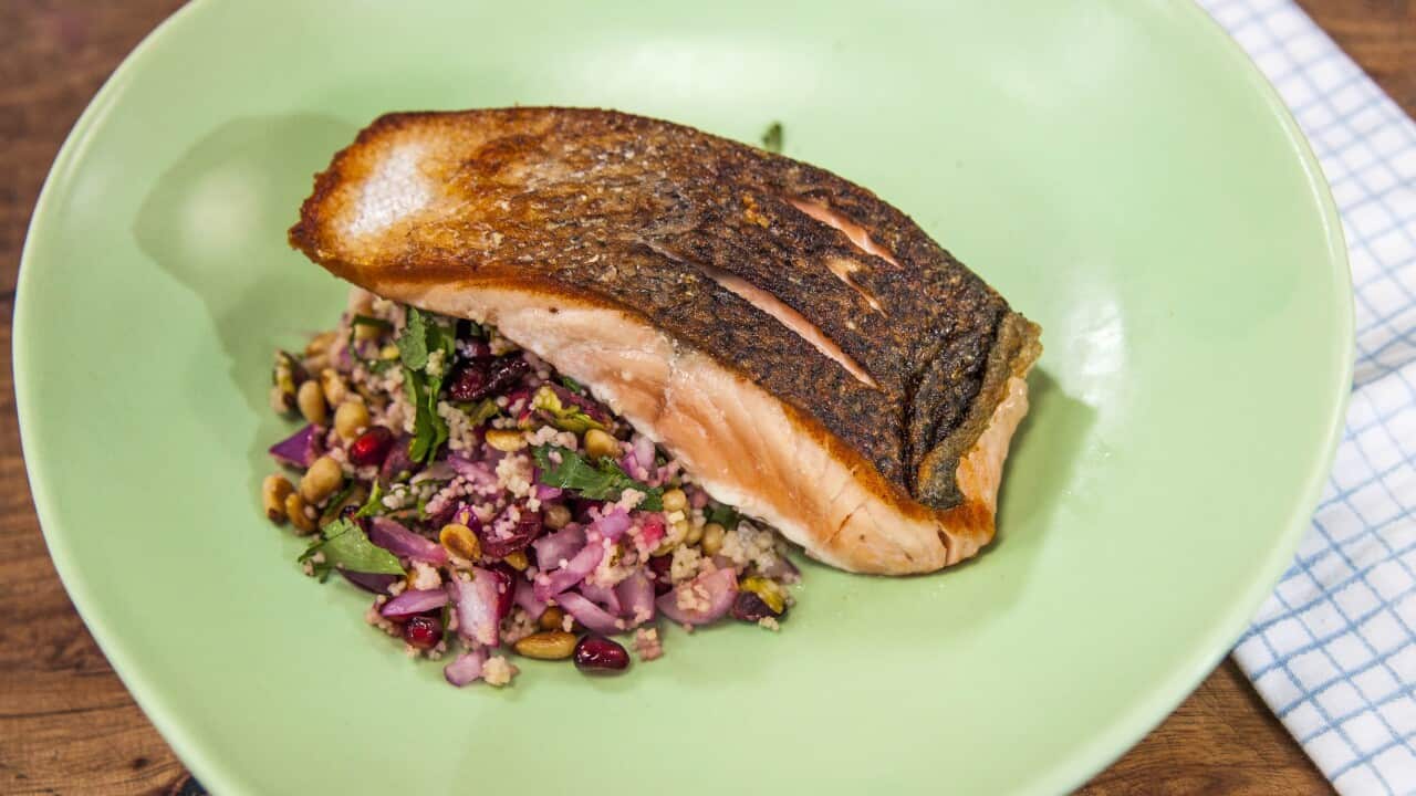 A salmon fillet sits beside a bed of couscous on a light green plate.