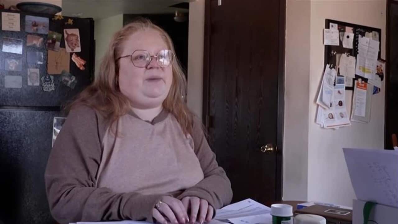 Sarah, who was diagnosed with breast cancer in 2020 sits at a table covered by papers from her health insurer, United Healthcare, bottles of prescription medication and her phone.