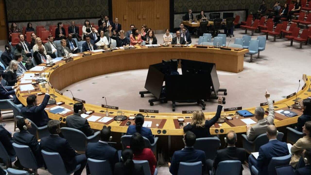 Members of the UN Security Council raise their hands to vote during a meeting at the council chamber.