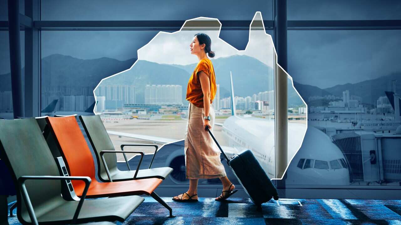 A woman with a rolling suitcase walks through an airport, with a plane visible in the background.