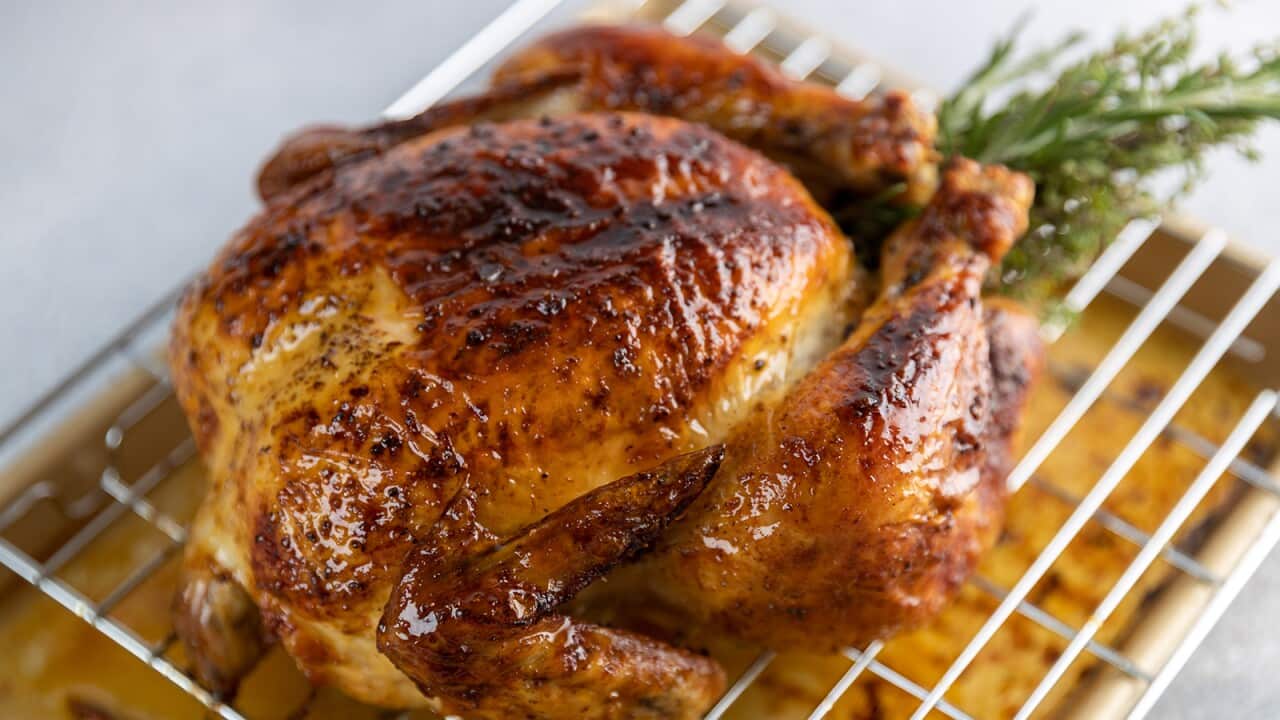 A golden brown roast chicken sits on a rack over a silver baking tray.